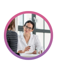 A woman sitting at a table, smiling and taking notes while another woman talks to her